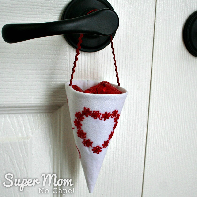 White Fabric Treat Cone with red embroidered floral heart hanging on a black door knob on a white door 