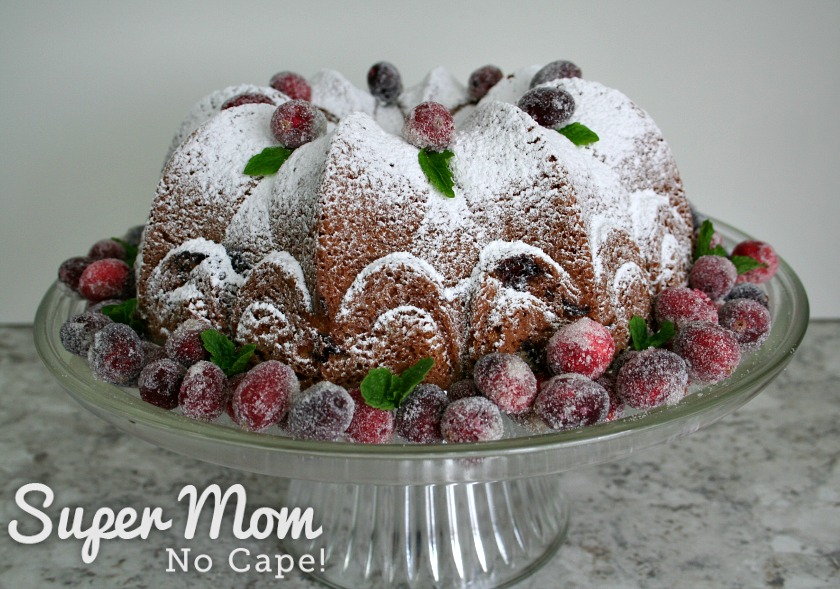 Cranberry Coffee Cake decorated with sugared cranberries and mint leaves on glass cake stand