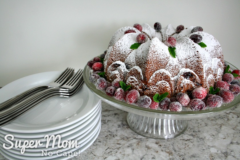 Cake stand with Cranberry Coffee Cake sitting beside a stack of plates and forks