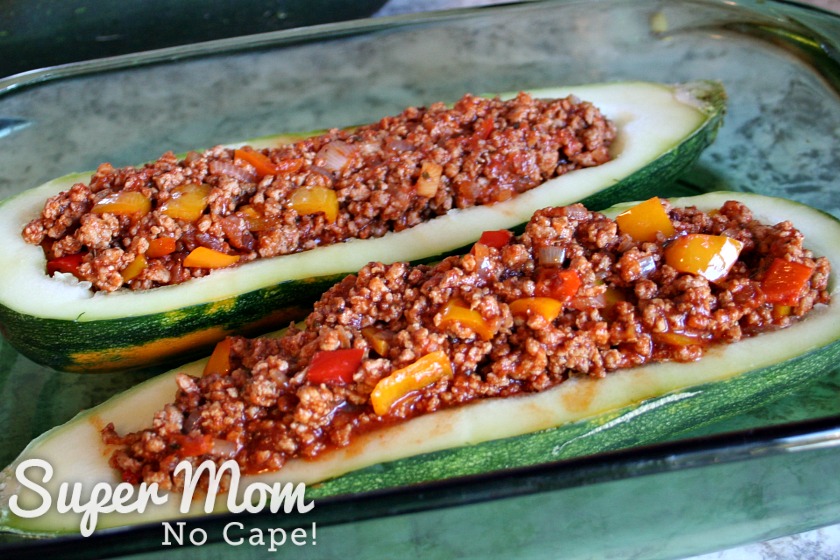 Two halves of a hollowed out zucchini with meat filling in a baking dish