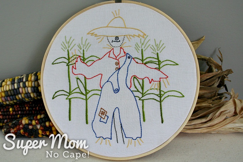 Scarecrow embroidery leaned against dried corn cobs