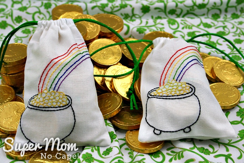 Two full drawstring bags filled with gold wrapped chocolate coins laying on a pile of gold chocolate coins.