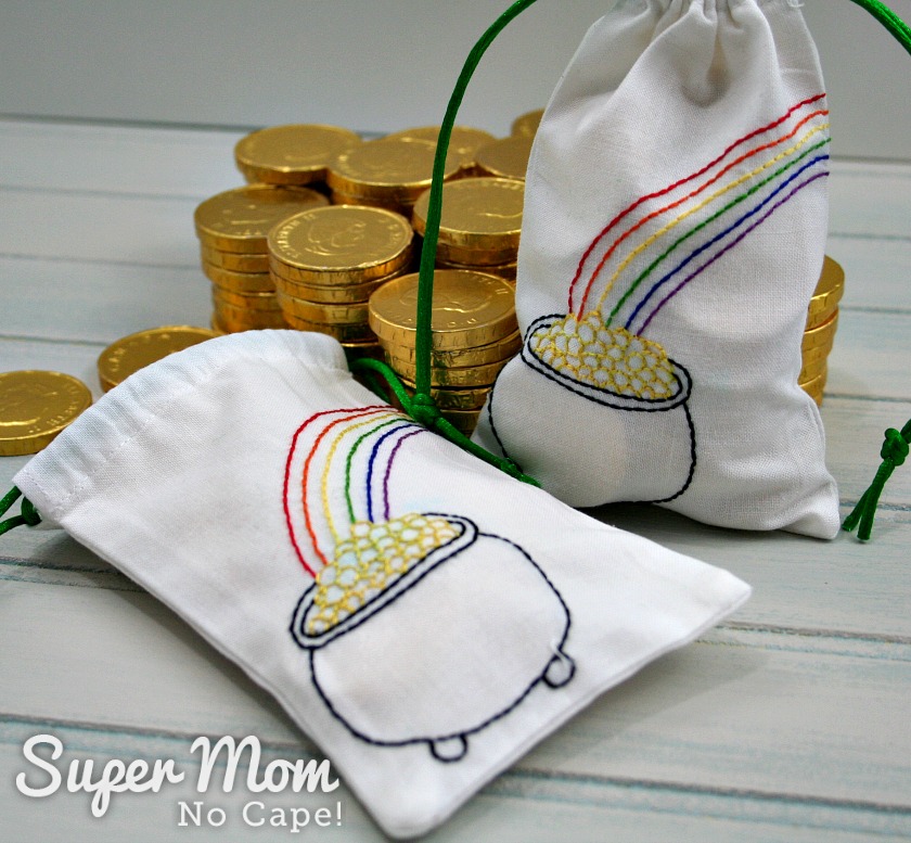 One embroidered bag filled with chocolate coins and a second bag half filled with coins behind both.