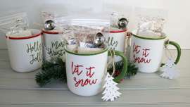 A picture of five tea mugs with bags of loose leaf tea stuffed inside. Each mug has a wooden Christmas Tree-shaped ornament tied to the handle.