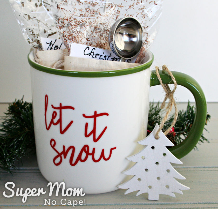 A picture of a tea mug with loose leaf tea in bags inside. On the handle of the mug is a wooden Christmas tree-shaped ornament